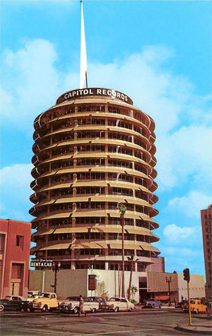 Vintage day shot of the famous tall, cylindrical building (inscribed with CAPITOL RECORDS at the top of the building) with many antique cars parked in the lot below.