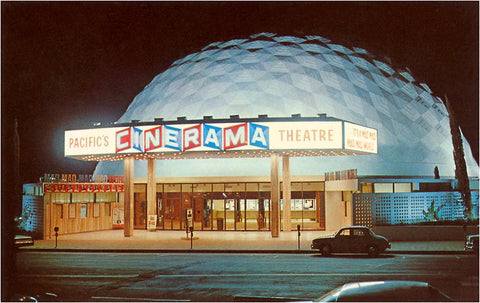 Nighttime image of vintage cars parked in front of a dome shaped building. The sign on the front of the building reads "Pacific's Cinema Theatre" in red, blue, and white blocks and writing.